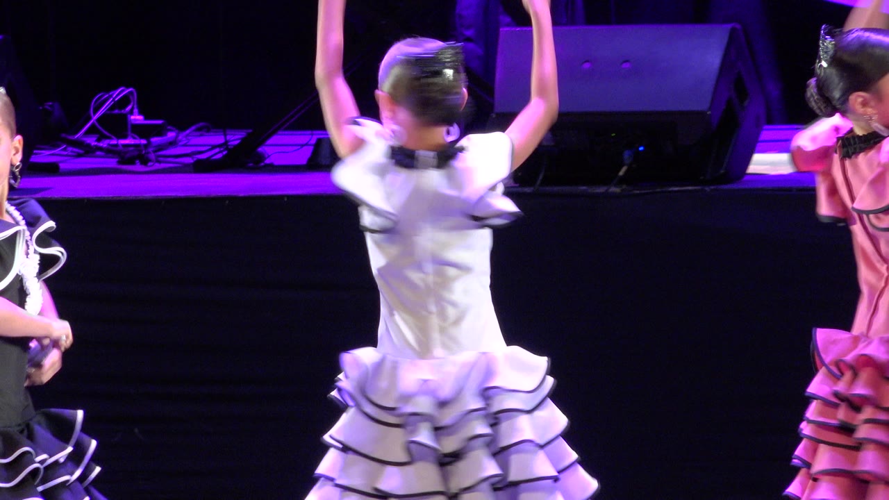 Girls in ruffled dance dresses on a purple-lit stage.