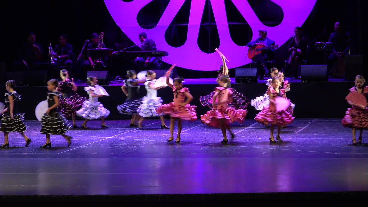 Girls in ruffled dresses dance on a purple-lit stage.