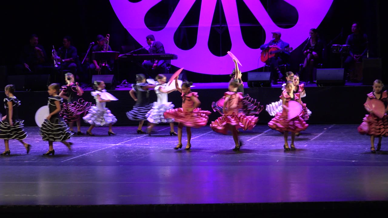 At 0:01, the dancers shift positions near center stage while the magenta circular backdrop and shadowed band remain visible behind them in Cabo San Lucas, Mexico.