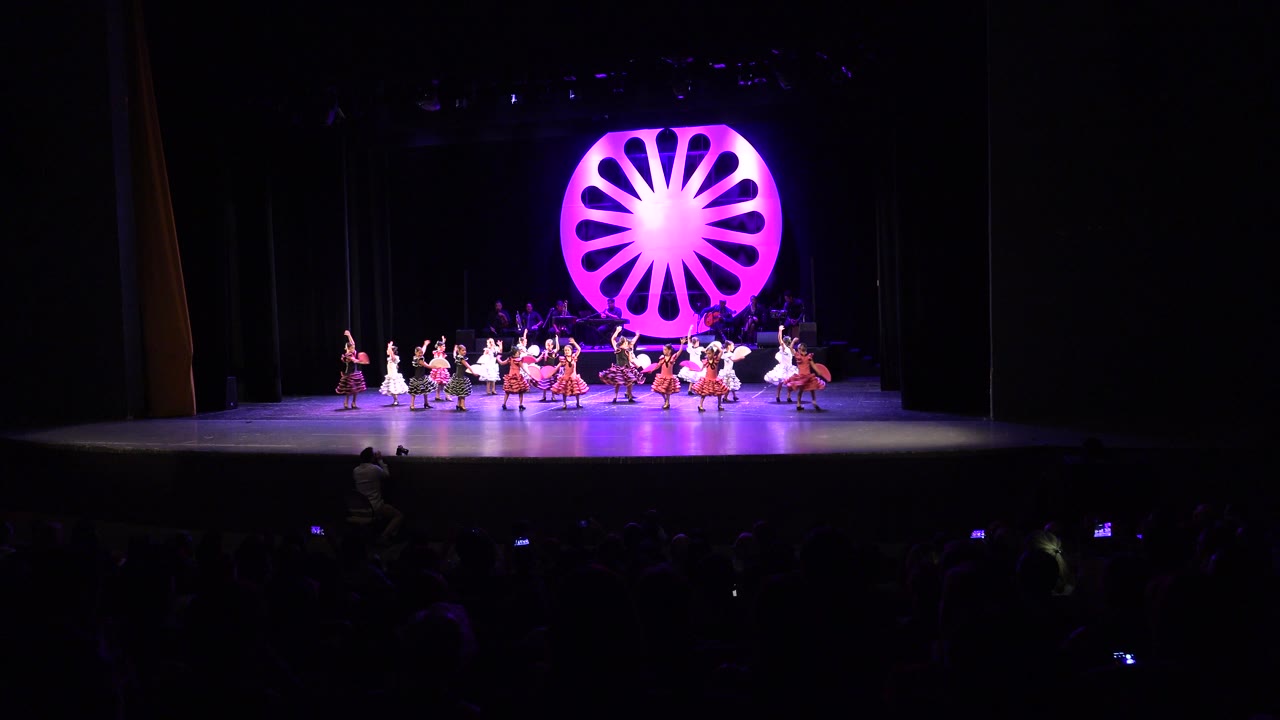 Dance group moves across stage in front of bright pink backdrop