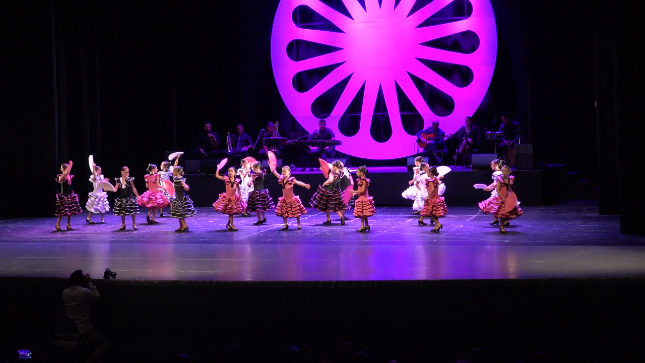 Children dancing on a stage beneath a large purple fan-shaped backdrop.