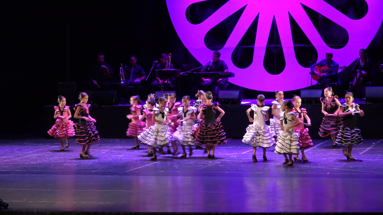Children in ruffled dresses gather on a purple-lit stage.