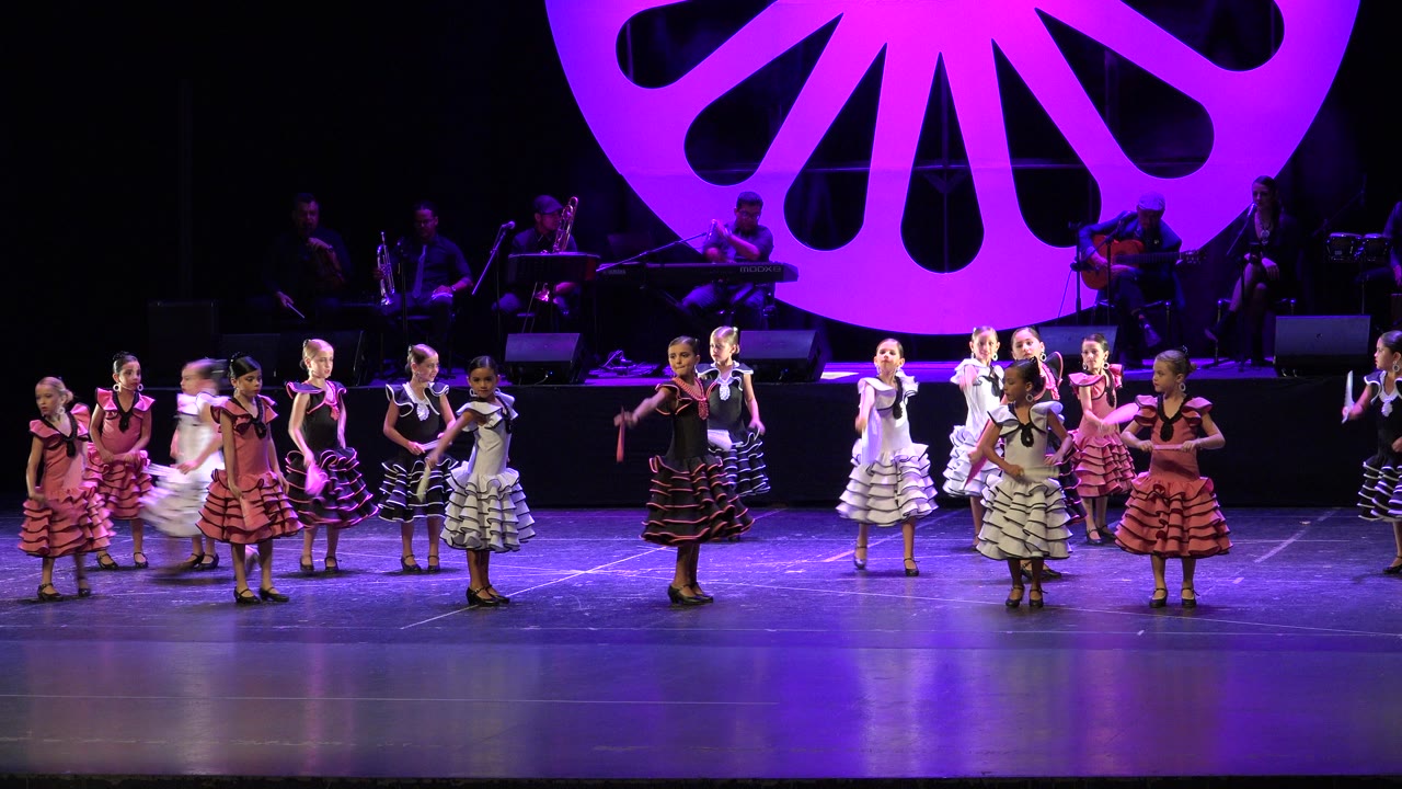 The dance formation holds across the stage in Cabo San Lucas, Mexico, with several performers facing forward and fans visible at chest height.