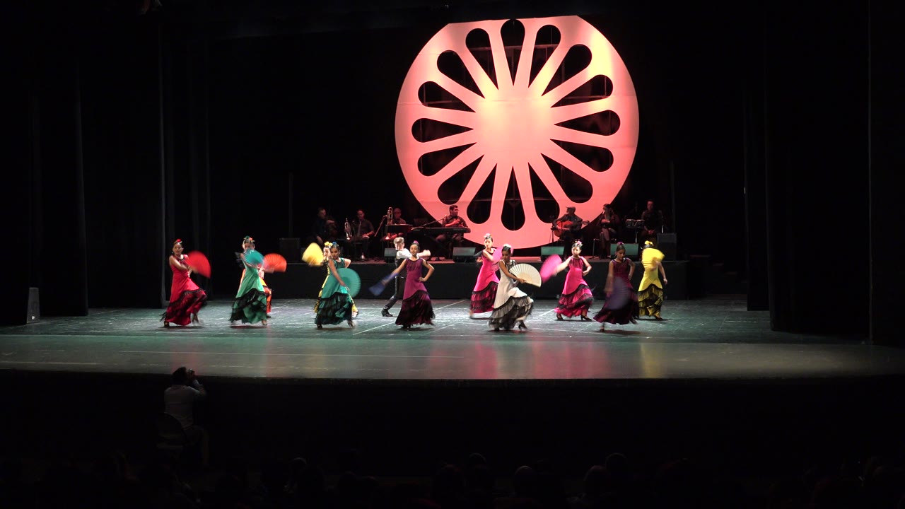 Wide theater stage with dancers and a glowing circular backdrop.