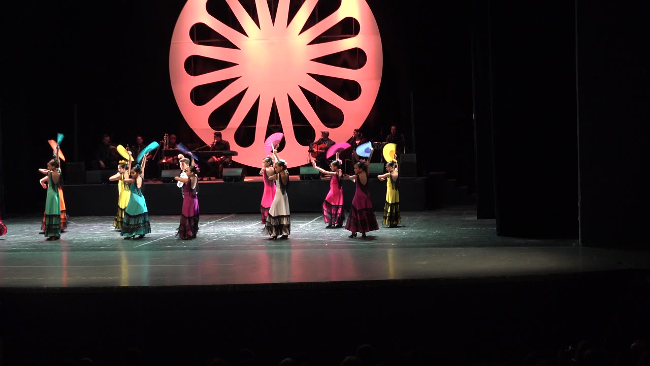 Children dance with colorful fans on a dark stage.