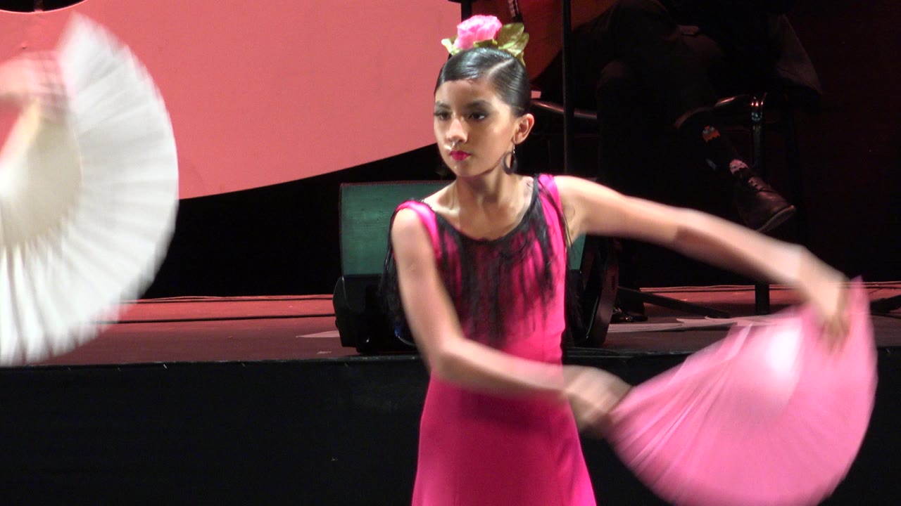 Girl in pink costume swings folding fans on a red-lit stage.