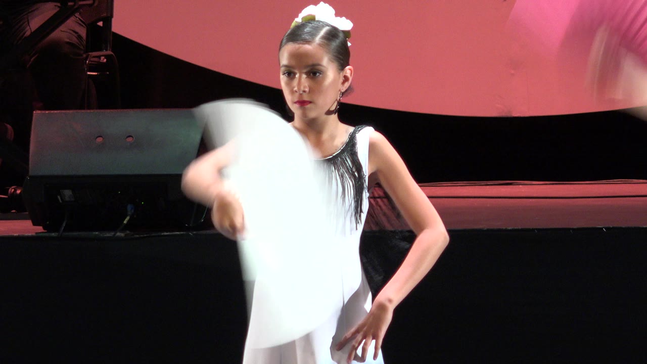 In Cabo San Lucas, Mexico, the dancer faces forward with a focused expression as the white fan blurs vertically in front of her costume.
