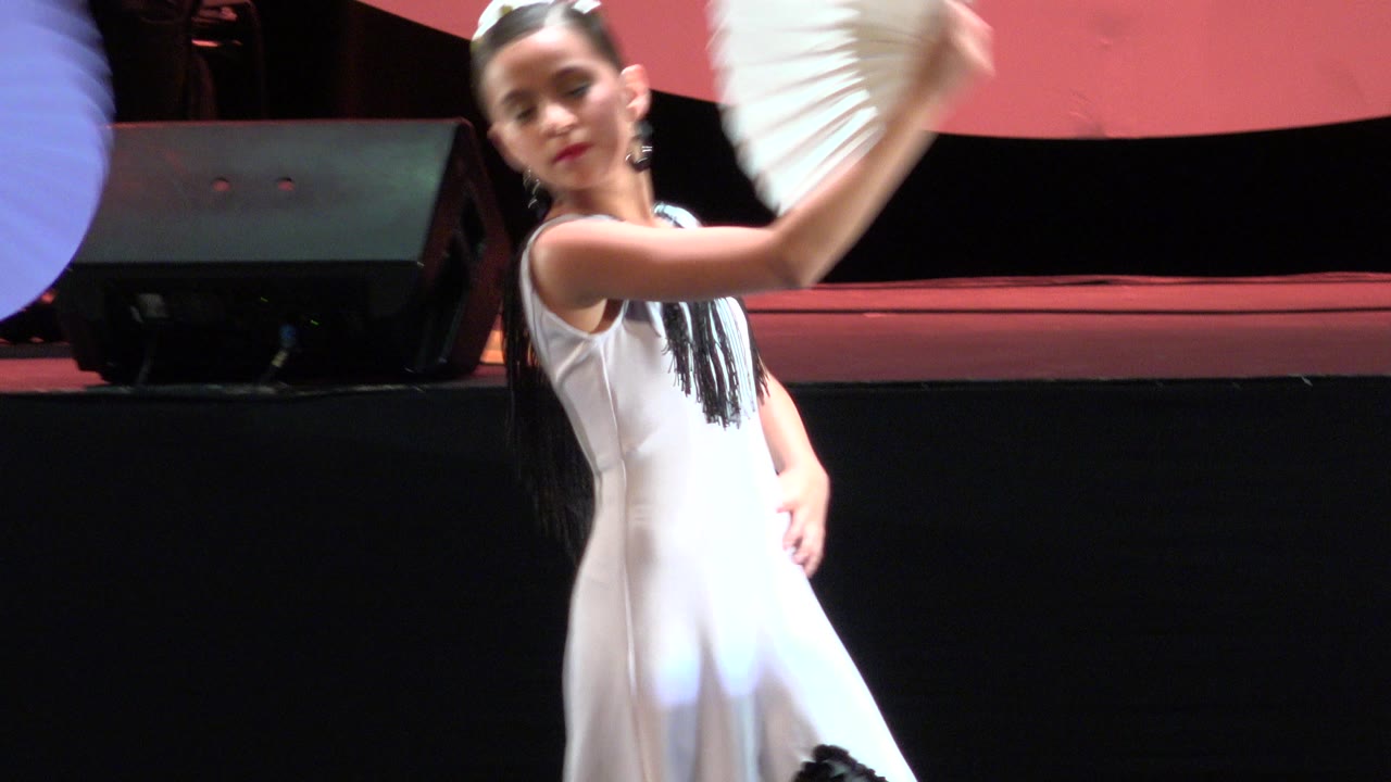 Girl in a white dress raises a white paper fan on stage.