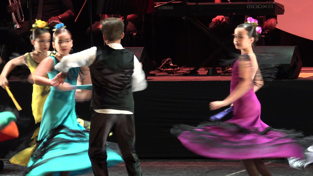 Children dance in a cluster with bright fans and spinning skirts.