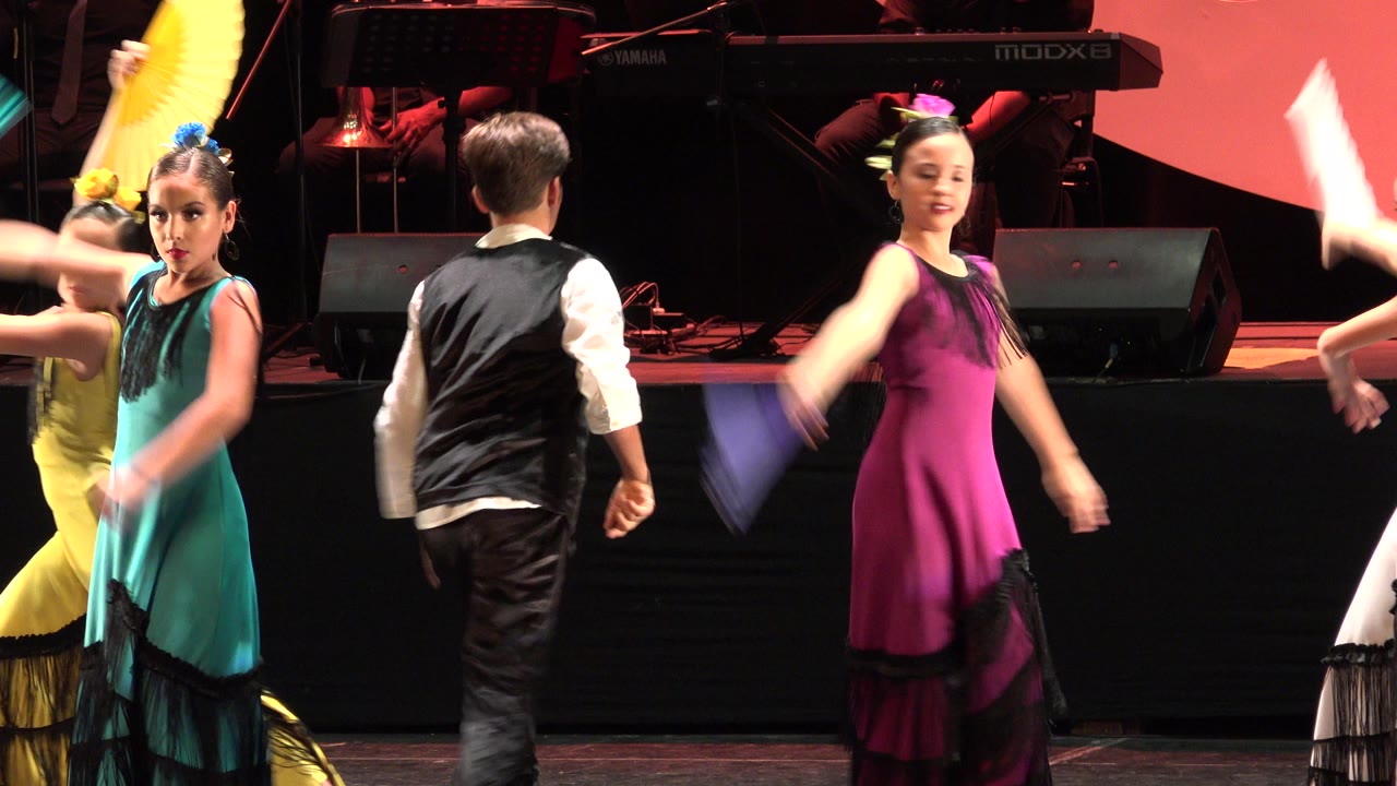 Children in colorful costumes dancing on a stage.