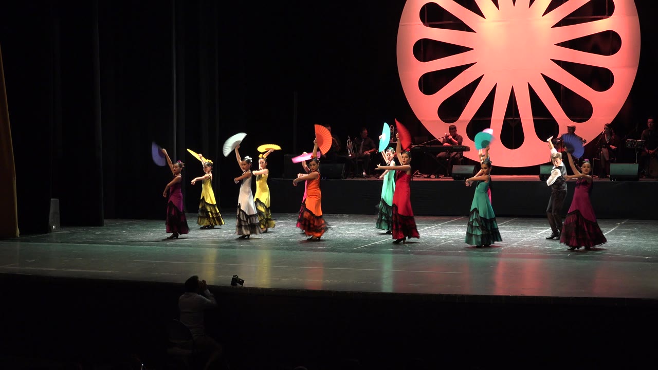 Colorful dance group crossing the stage with fans held overhead.