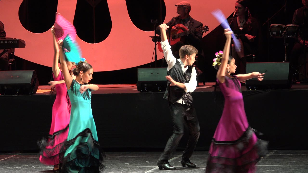 Children raise fans while dancing in front of musicians on a stage.