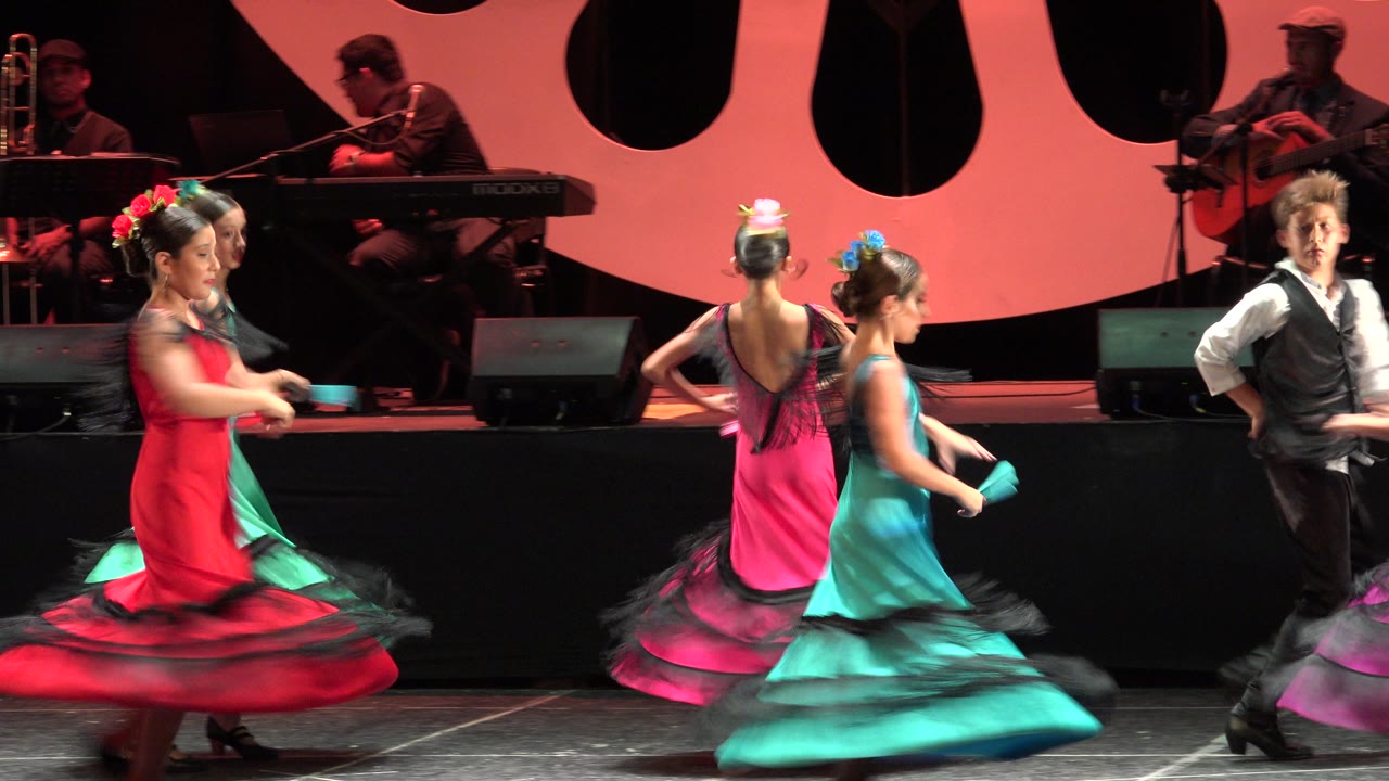 Dancers spin with skirts flaring in front of a live band on stage.
