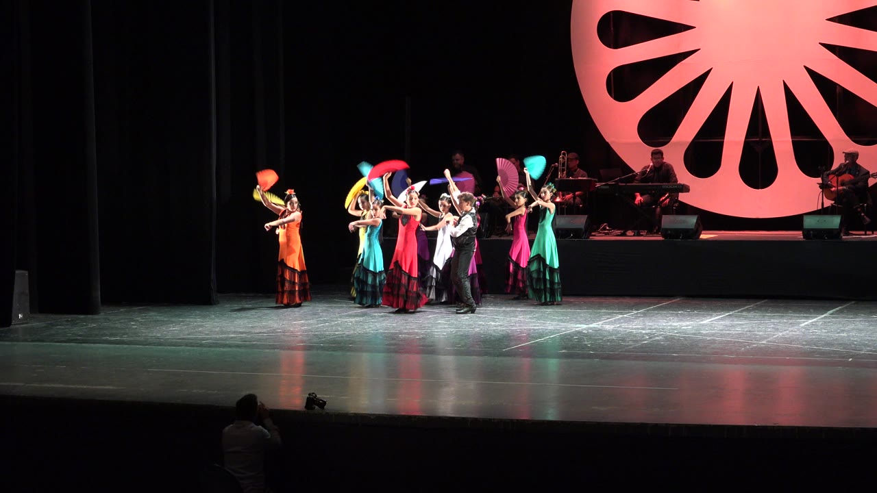 Young dancers grouped on a theater stage with colorful fans and costumes.