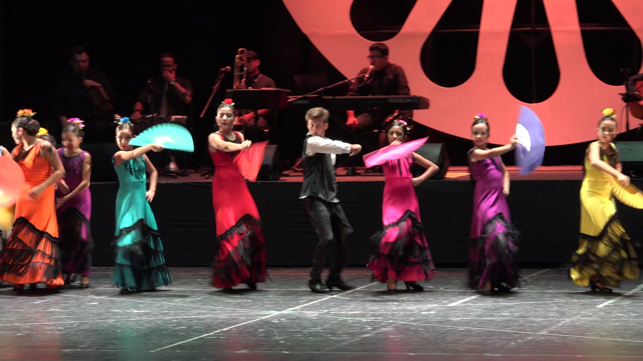 Dancers on stage hold colorful paper fans during a group routine.
