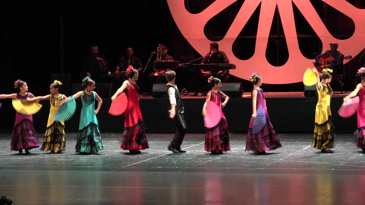Dance ensemble turns on stage with fans extended.