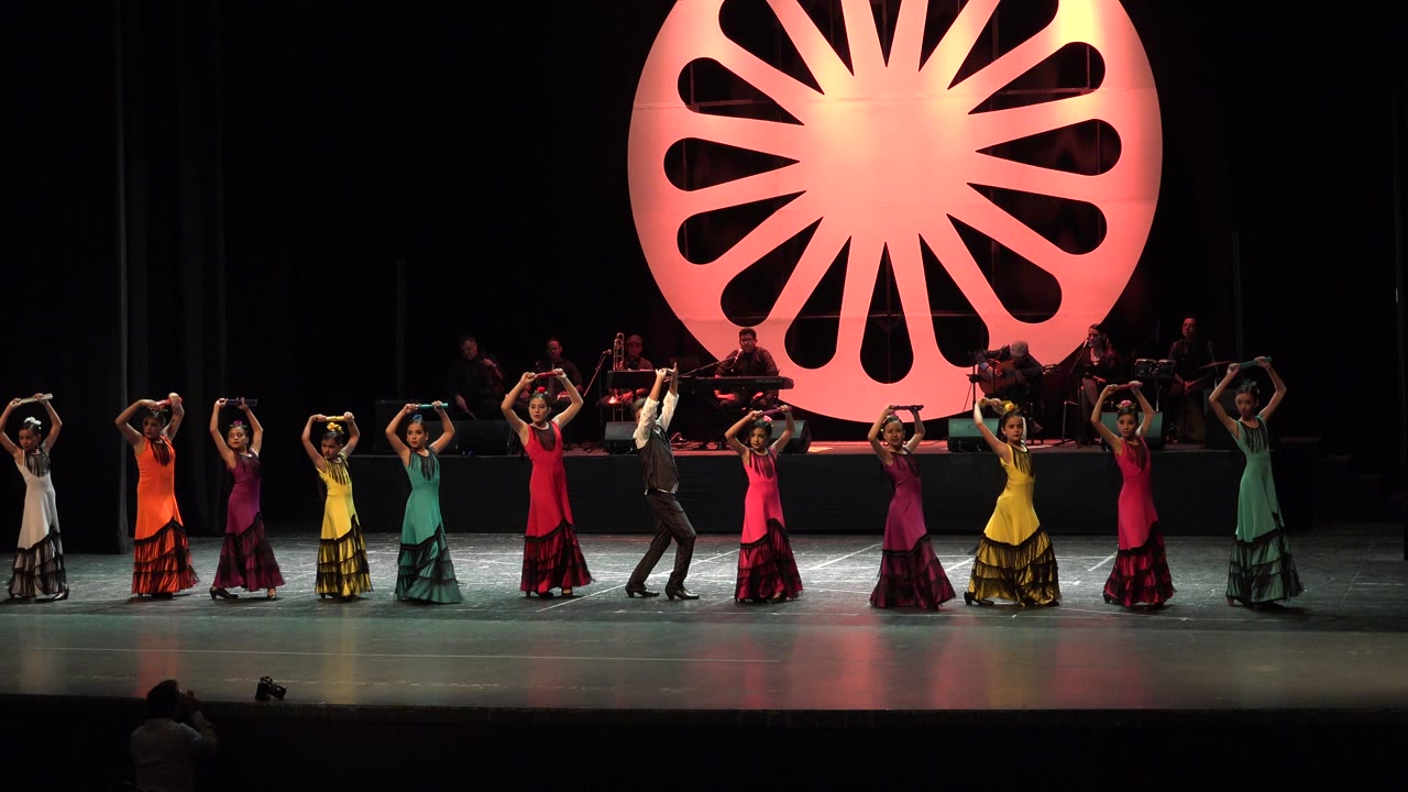 Dancers lined across a stage beneath a glowing circular backdrop.