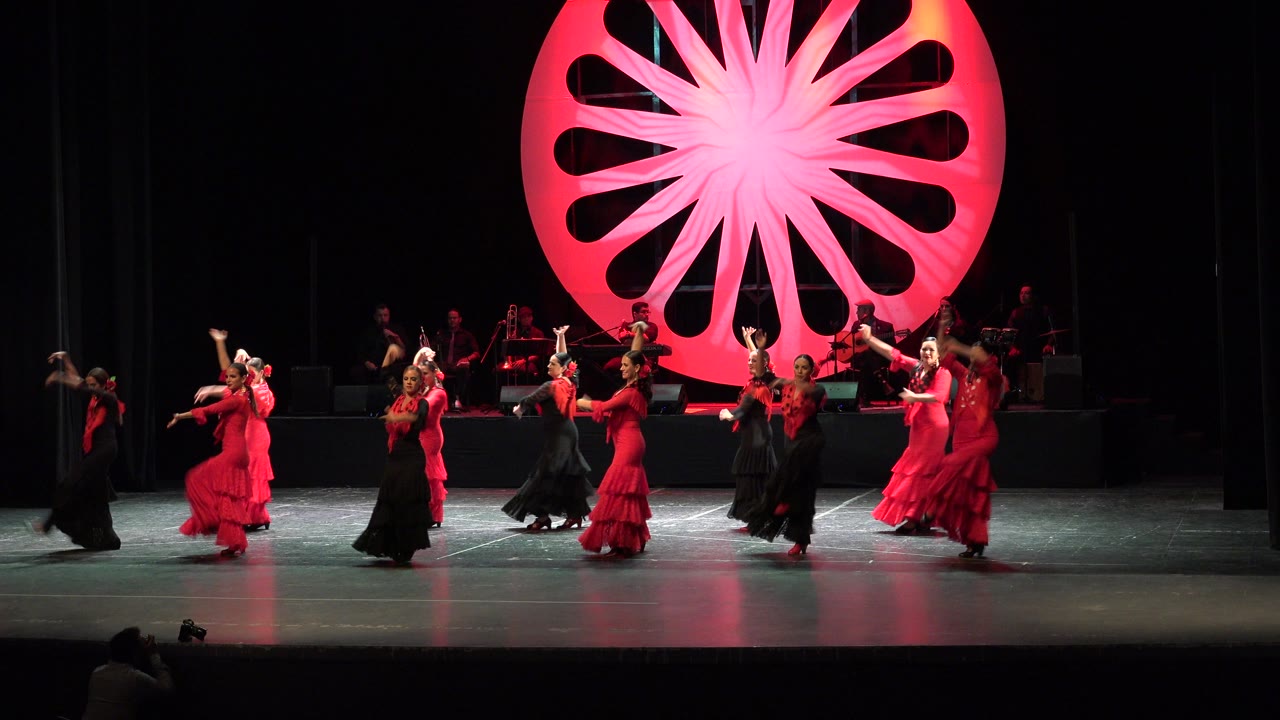 Women in red and black dresses dancing on a theater stage.