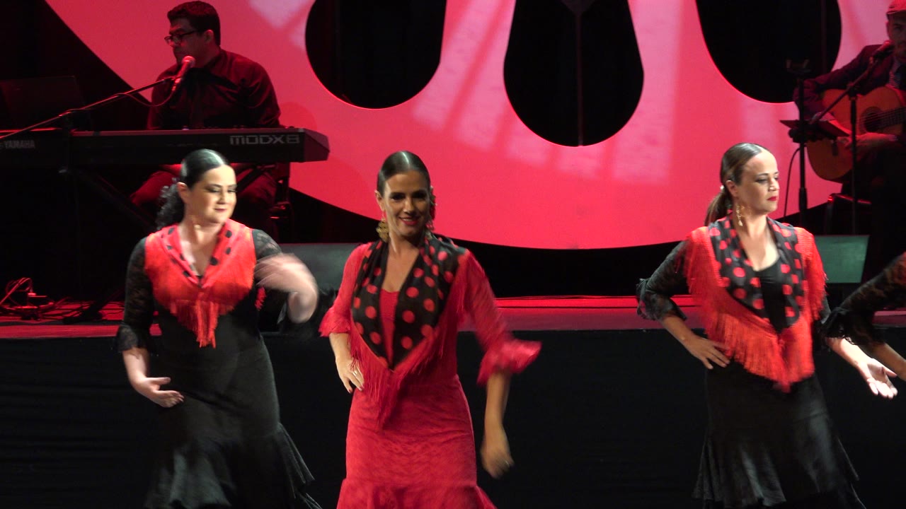 Two women dancing on a red-lit stage with a keyboard player behind them.