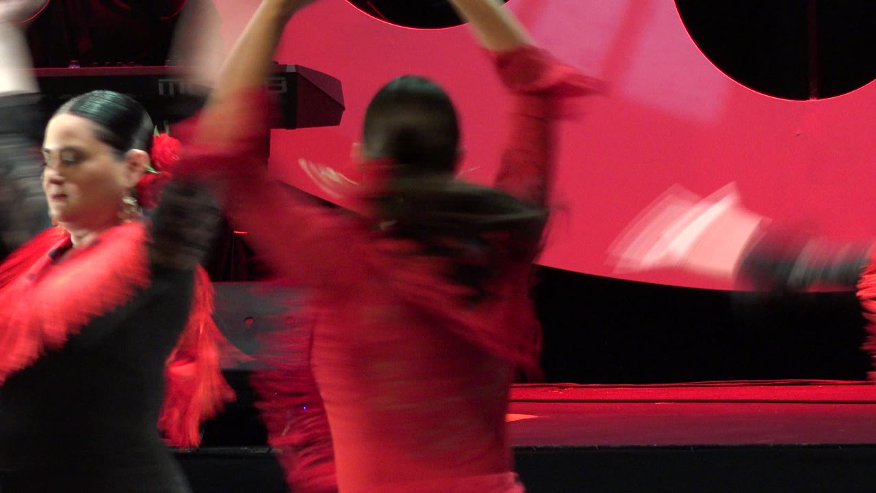 Two women dancing on a red-lit indoor stage with motion-blurred arms.