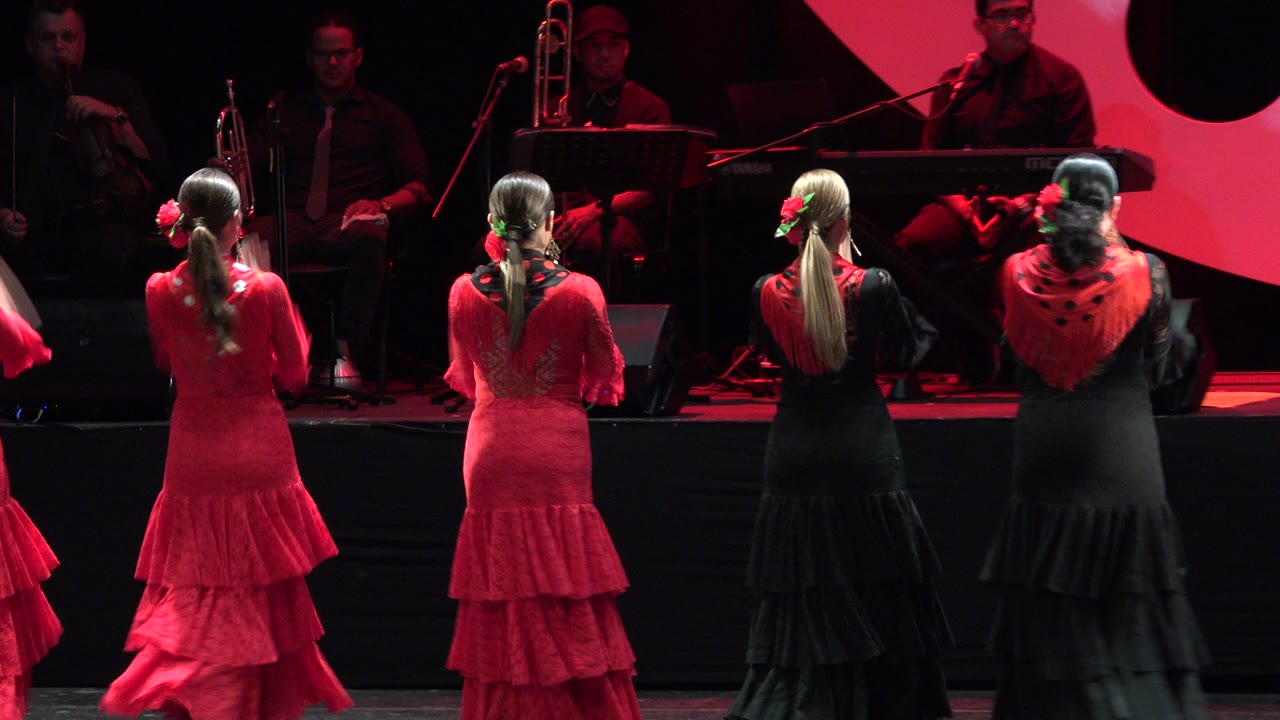 In Cabo San Lucas, Mexico, the performers hold a rear-facing formation in red and black flamenco dresses while musicians sit in the dim background.