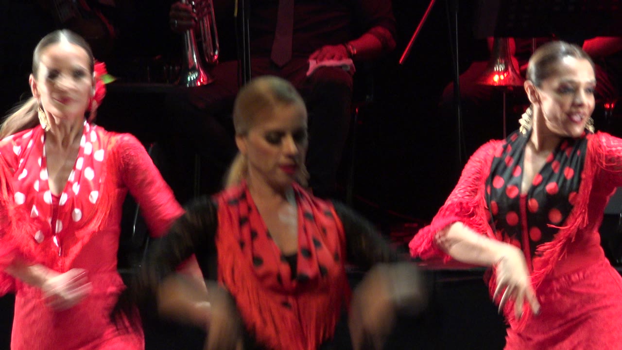 At 0:01 in Cabo San Lucas, three women fill the frame in coordinated red and black outfits, with the center dancer facing forward and the others moving at the sides.