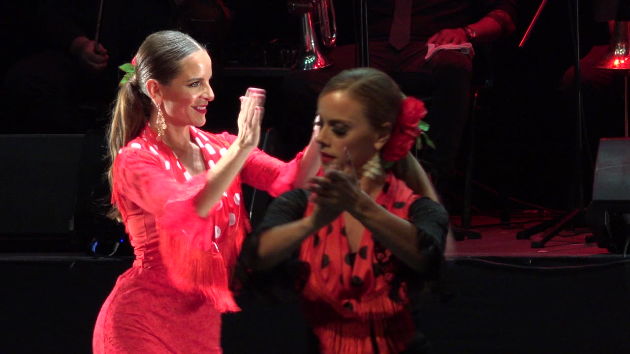 Two women in red stage costumes clap during a performance.