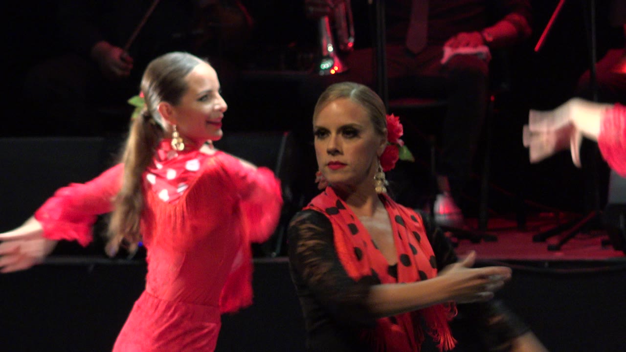 Two women in red and black dance costumes on a dark stage.