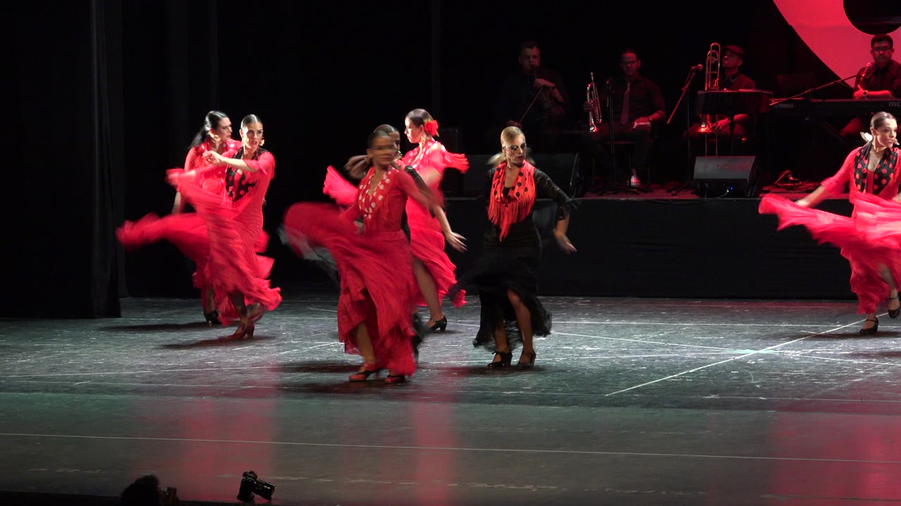 Women in red and black dance costumes performing on a stage.