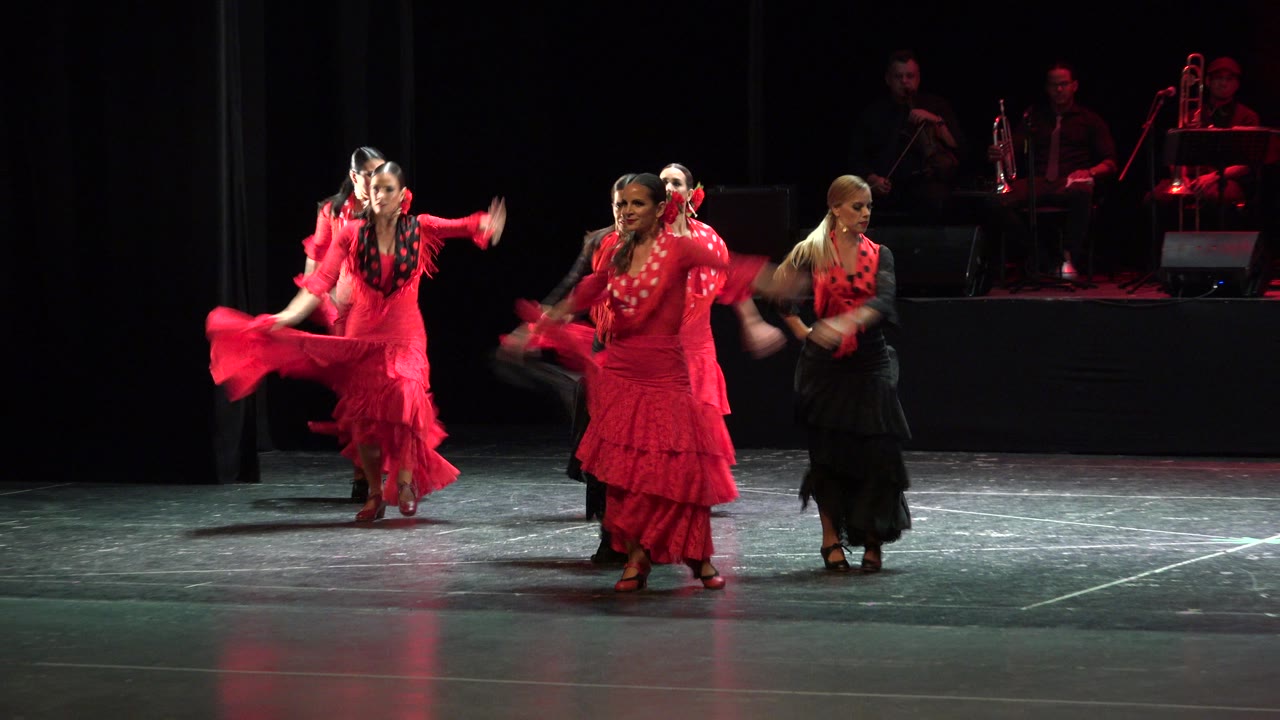 Women in red and black dresses dancing on a dark stage