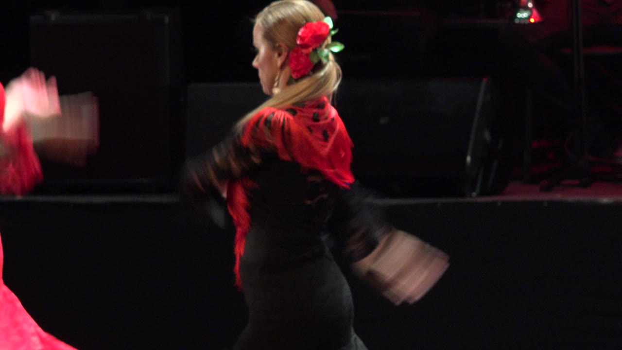 Woman in a black dress and red scarf dancing in profile on a dark stage.