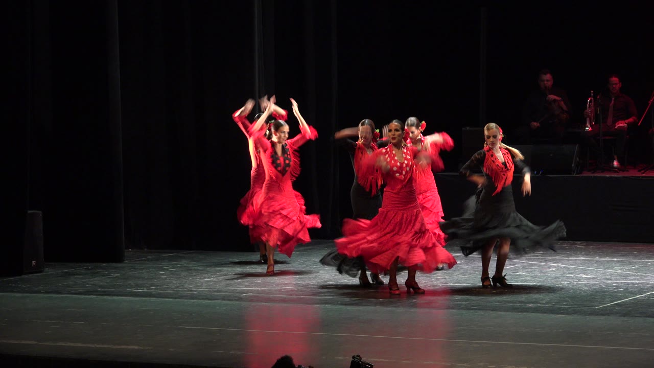 Dancers in red and black costumes perform on a dark stage.