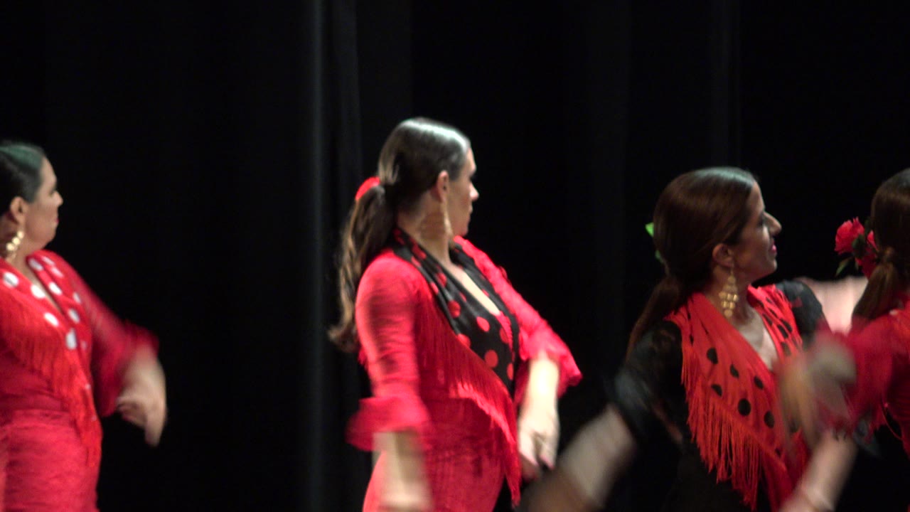 Women in red dance costumes face each other during a stage routine.