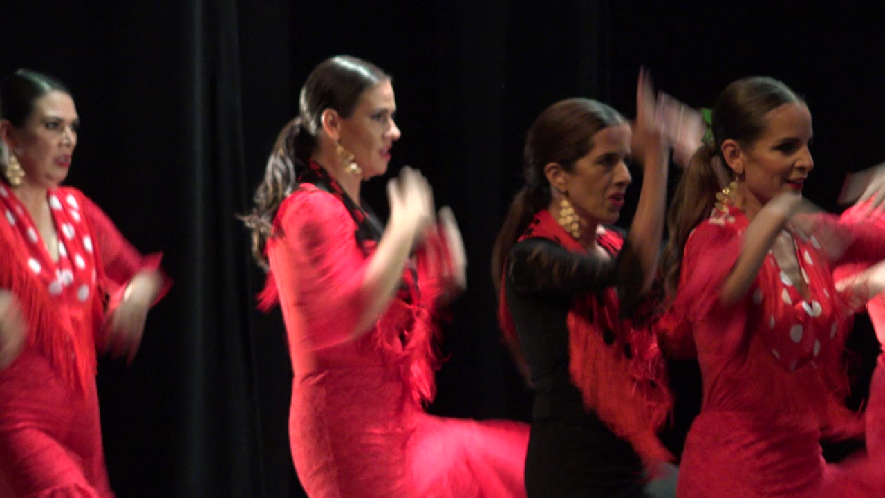 Women in red and black dance costumes clapping on a dark stage.