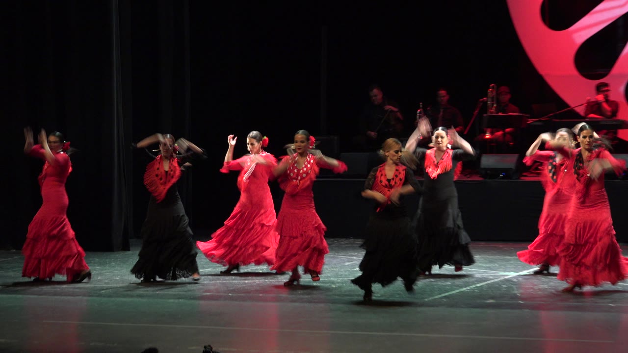 Dancers move across a stage with a red backdrop element.