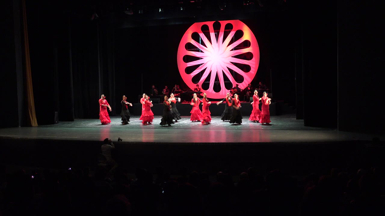 Women in red and black costumes dance on a theater stage.