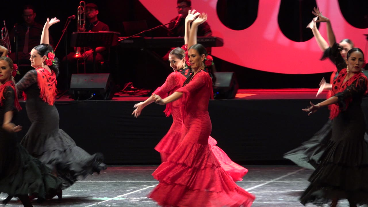 Two red-dressed flamenco dancers with black-dressed performers nearby