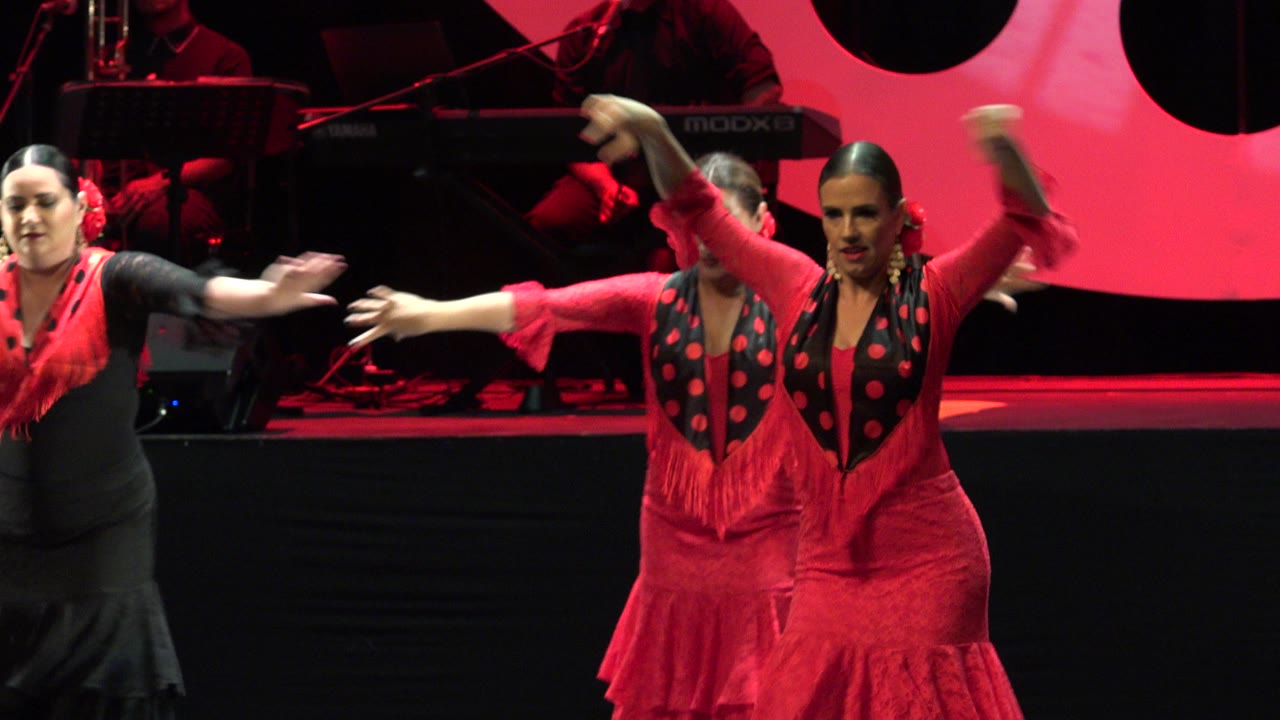 Women in red and black stage costumes dance under red lighting.