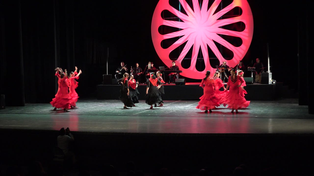 Wide theater stage with dancers in red and black costumes under a red circular backdrop.
