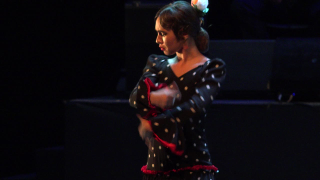 Young woman in polka dot dress dancing on a dark stage.