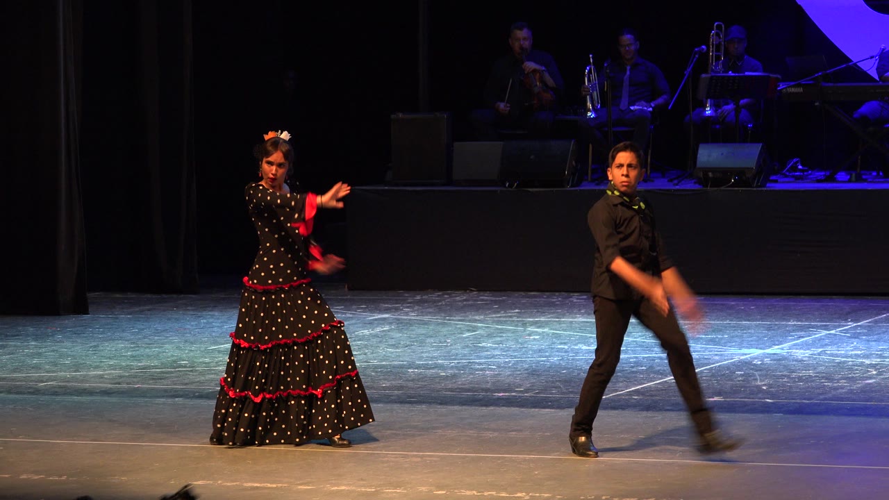 Adult dance duo on a theater stage with musicians behind them.