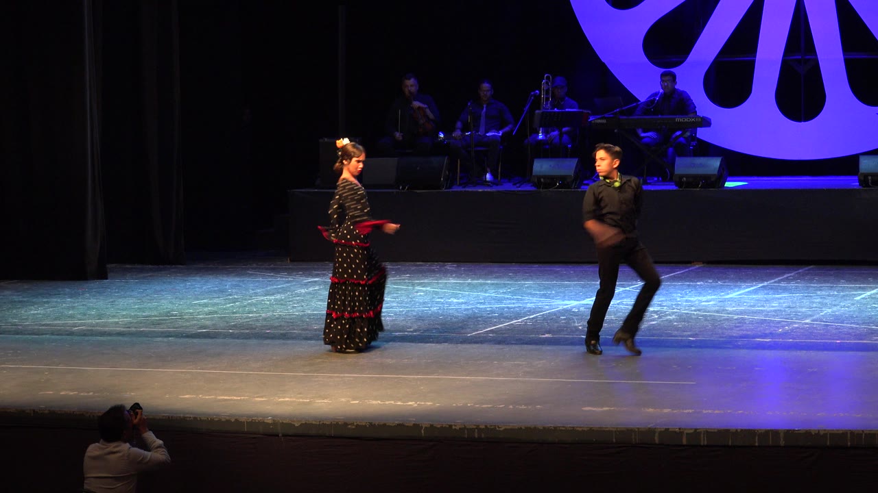 The girl holds a poised arm position while the boy steps toward her on the lit theater stage in Cabo San Lucas, Mexico.