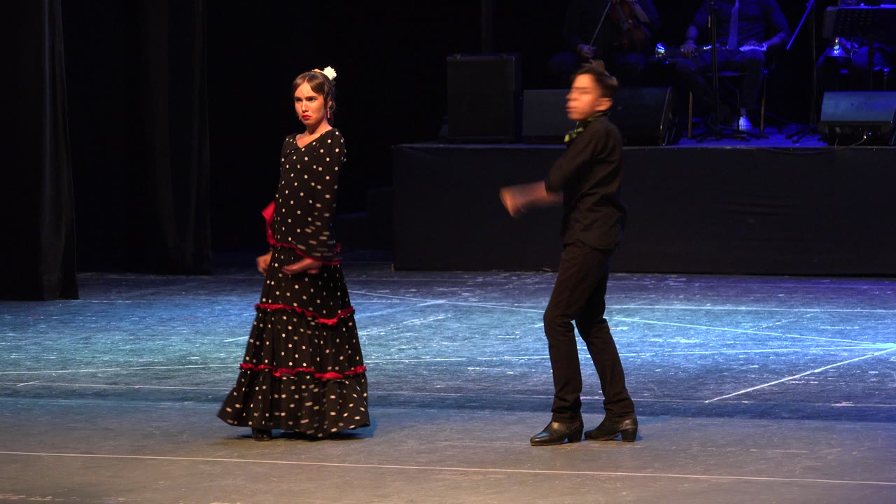 Two young dancers on a stage, one in a black dress with red trim and one in black clothing.