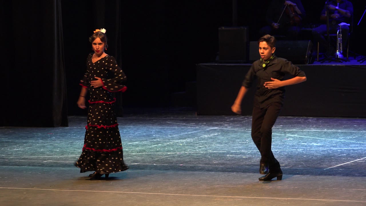 Two dancers stand on a theater stage under stage lights.