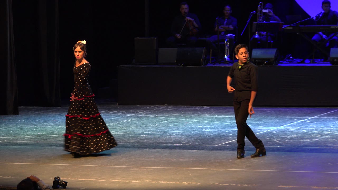 Two young dancers on a lit stage with musicians behind them.
