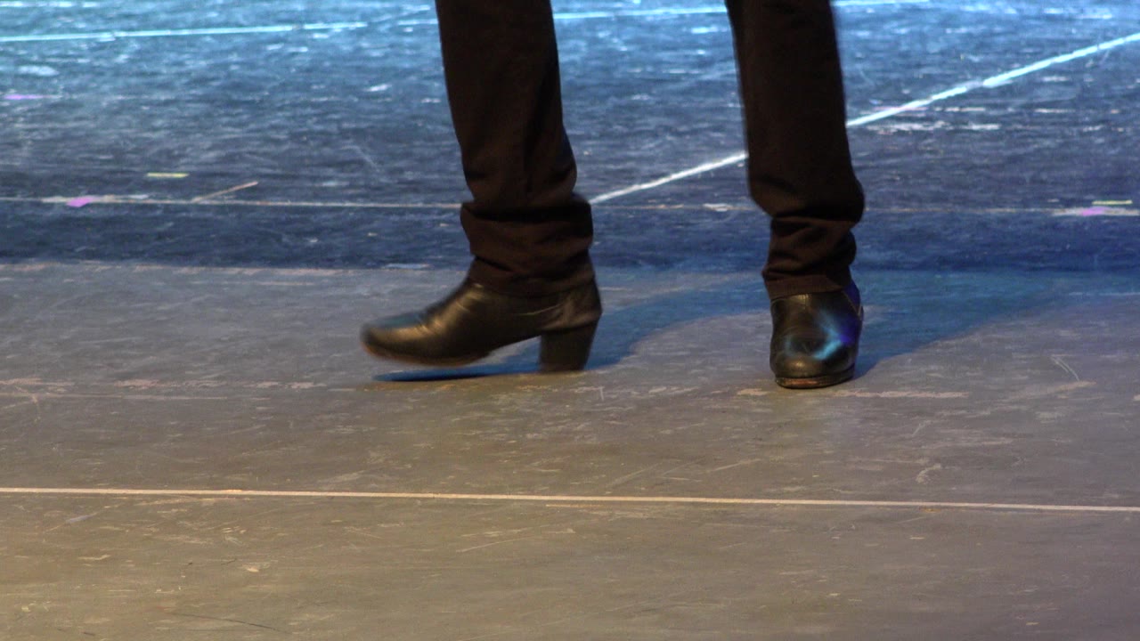Close-up of a dancer's black heeled shoes and black pants on a scuffed blue-lit stage floor in Cabo San Lucas, Mexico.