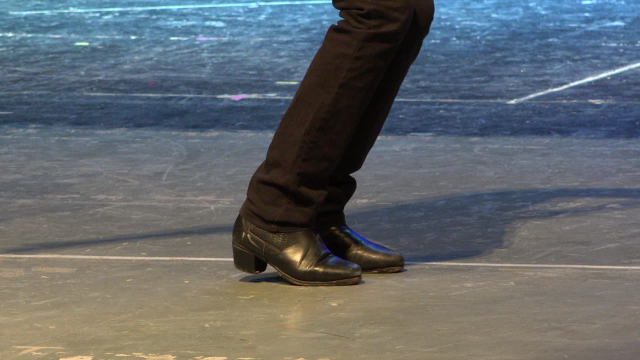 Black boots stepping on a scuffed stage floor.