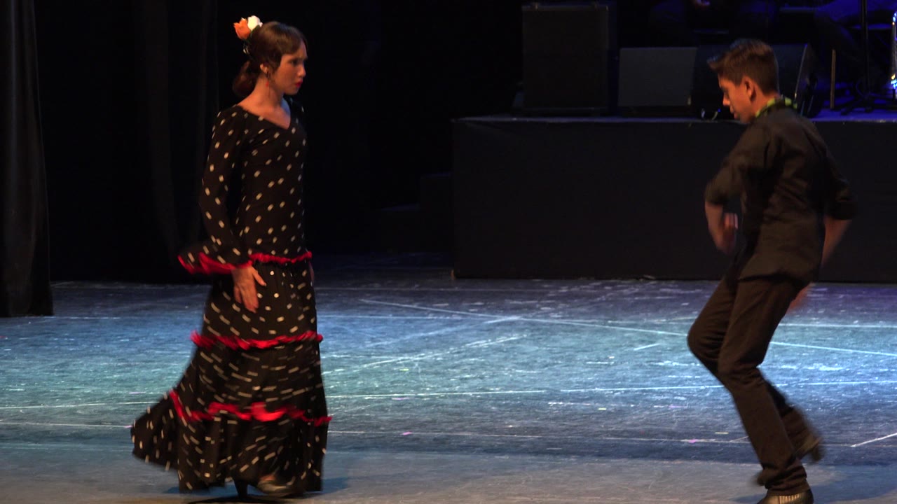 Teen boy and girl face each other on a stage during a Latin dance routine.