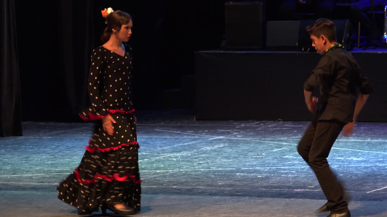 In Cabo San Lucas, Mexico, the girl remains poised at left while the boy steps with bent knees at right under blue-purple stage lighting.