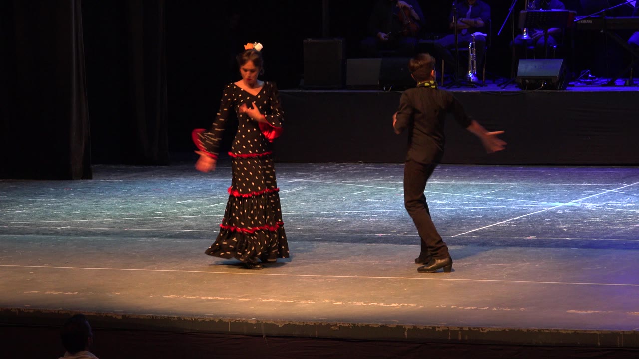 Woman in black and red dress dances opposite man in black on stage.